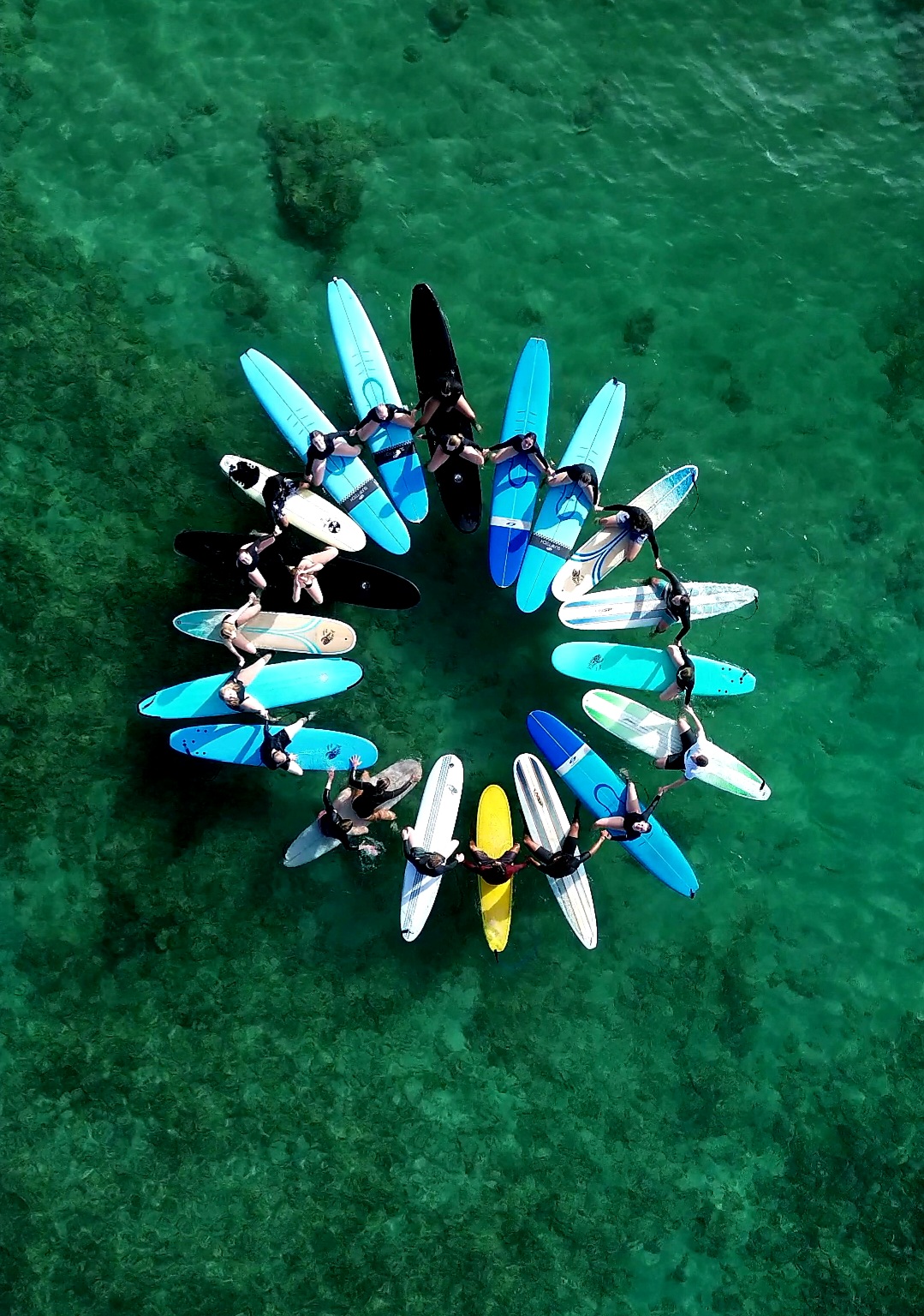 HI Surf Camp surfers forming a circle with their surfboards in clear Hawaiian water